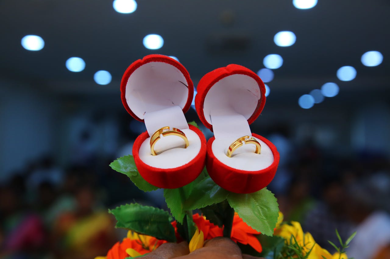 Close-up of gold wedding rings in red velvet boxes with floral accents, perfect for ceremonies.