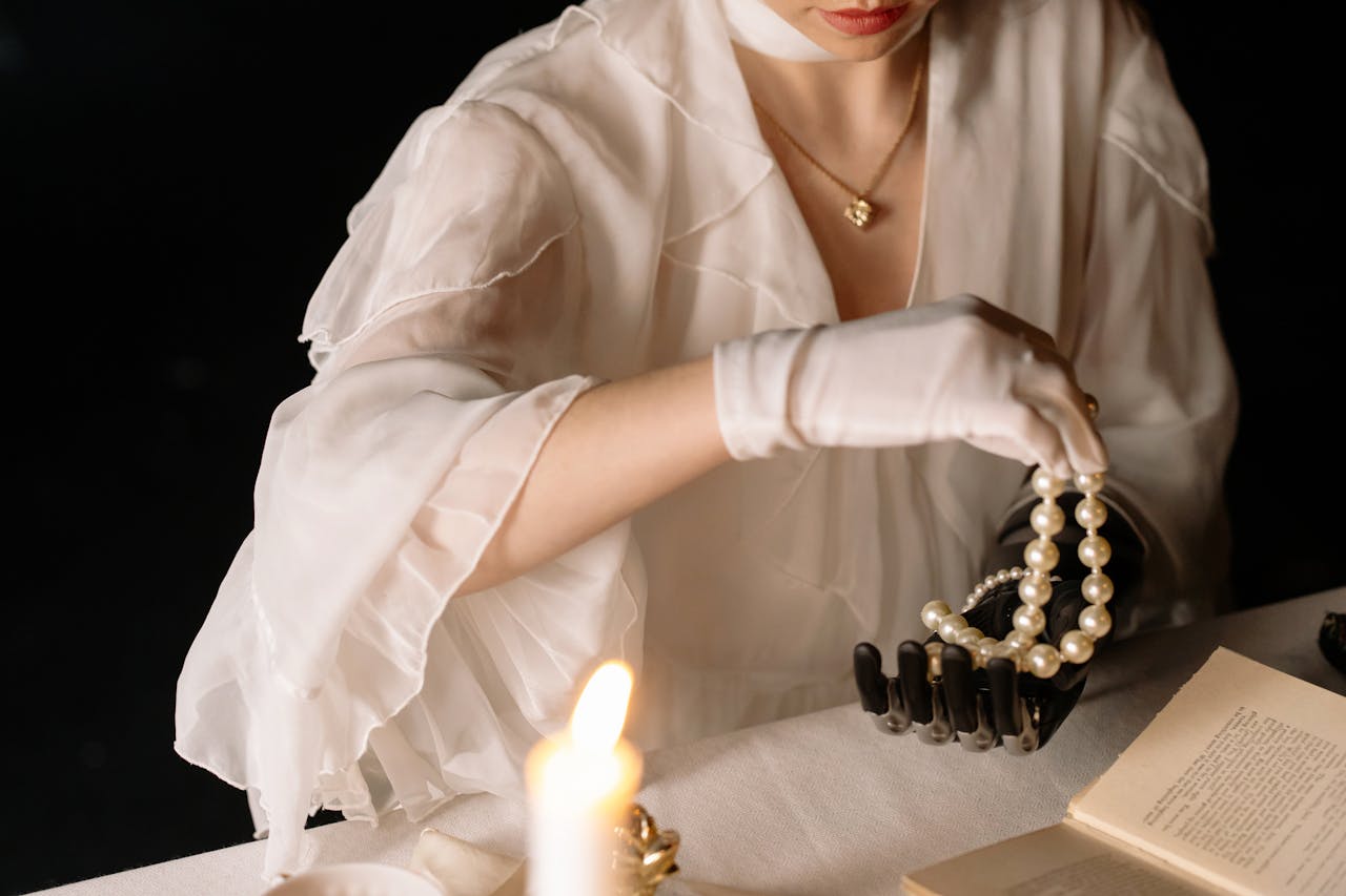 A prosthetic hand delicately holds a pearl necklace with a candlelit ambiance, blending elegance with technology.