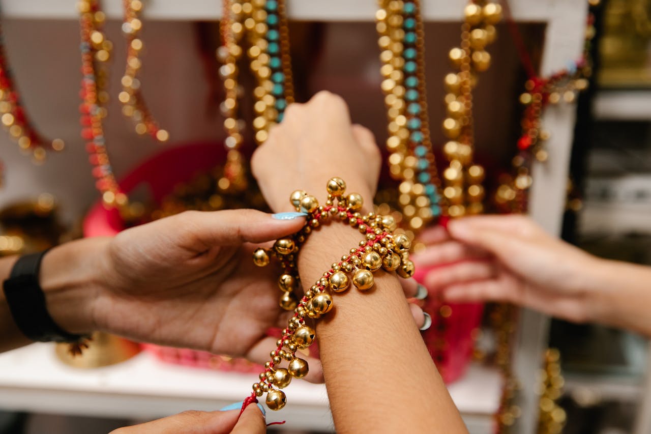 Hands arrange a vibrant gold and red beaded bracelet with colorful beads in the background.